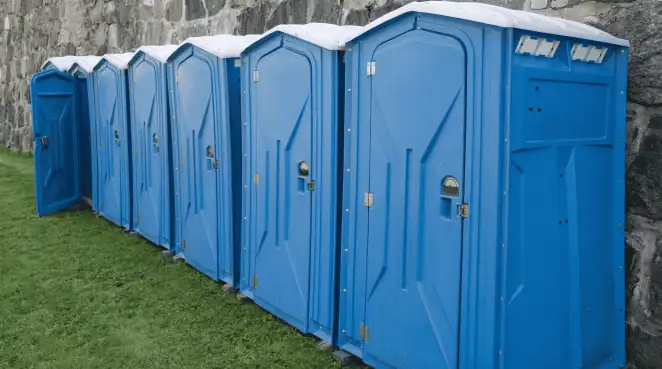 Row of blue portable toilets lined up on grass against a stone wall for event sanitation in Birmingham, AL