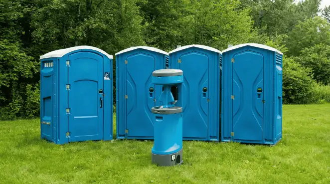 Four blue portable toilets and a matching hand washing station on grass near trees, a common sight at local outdoor events in Birmingham, AL