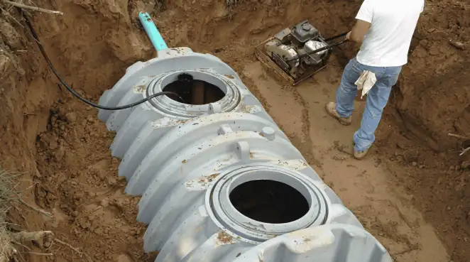 Septic tank installation showing a technician compacting soil around a new poly septic tank in an excavation pit in Birmingham, AL